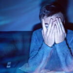 Man covering his eyes while watching TV.